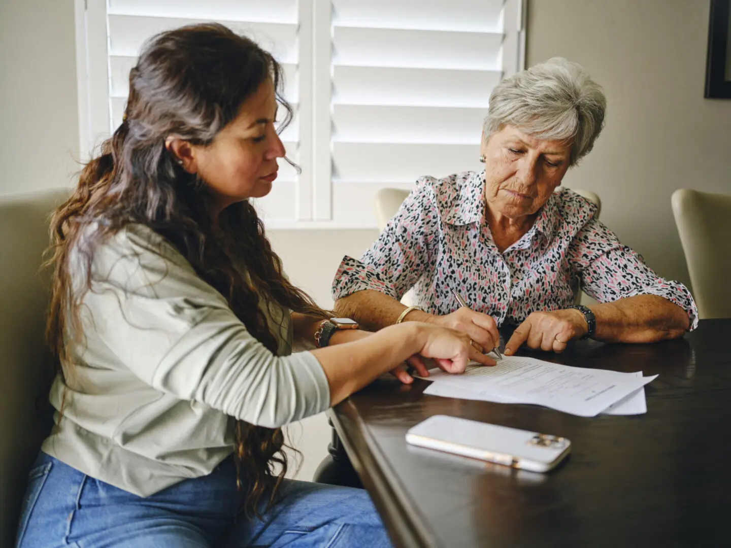 Caregiver helping elderly woman sign documents